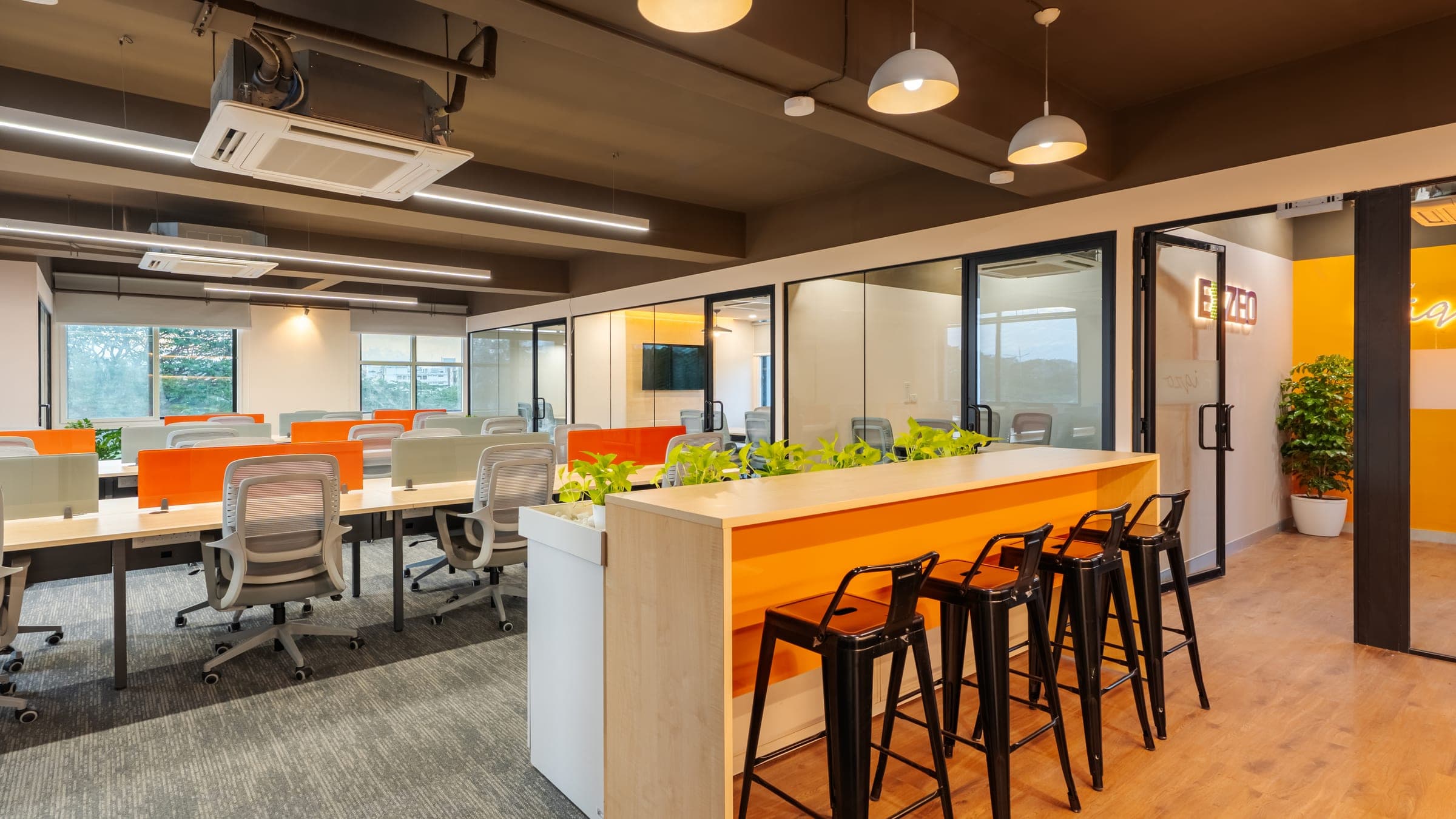 Planter bar with stools and pendant lights beside the Exzeo signage in the 50 seater managed office built by Fliqzo, Coimbatore