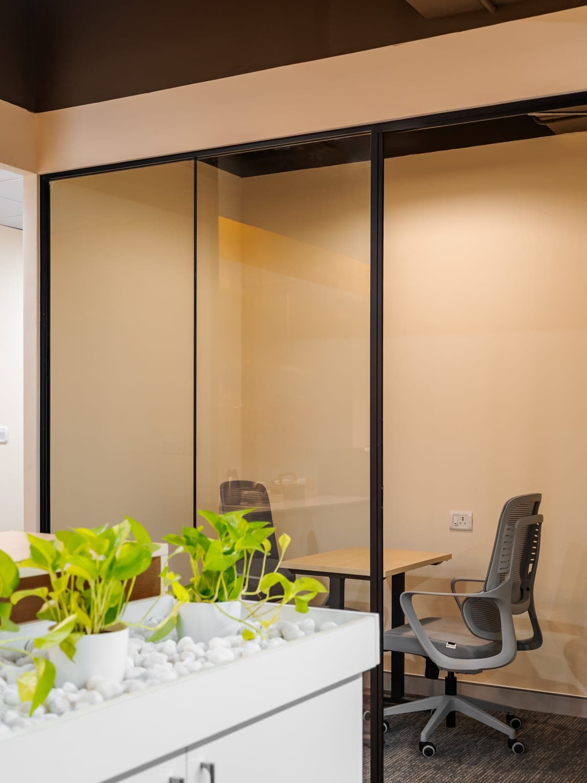 Glass-walled two seater phone room behind the planter bar in the Exzeo managed office built by Fliqzo, Coimbatore