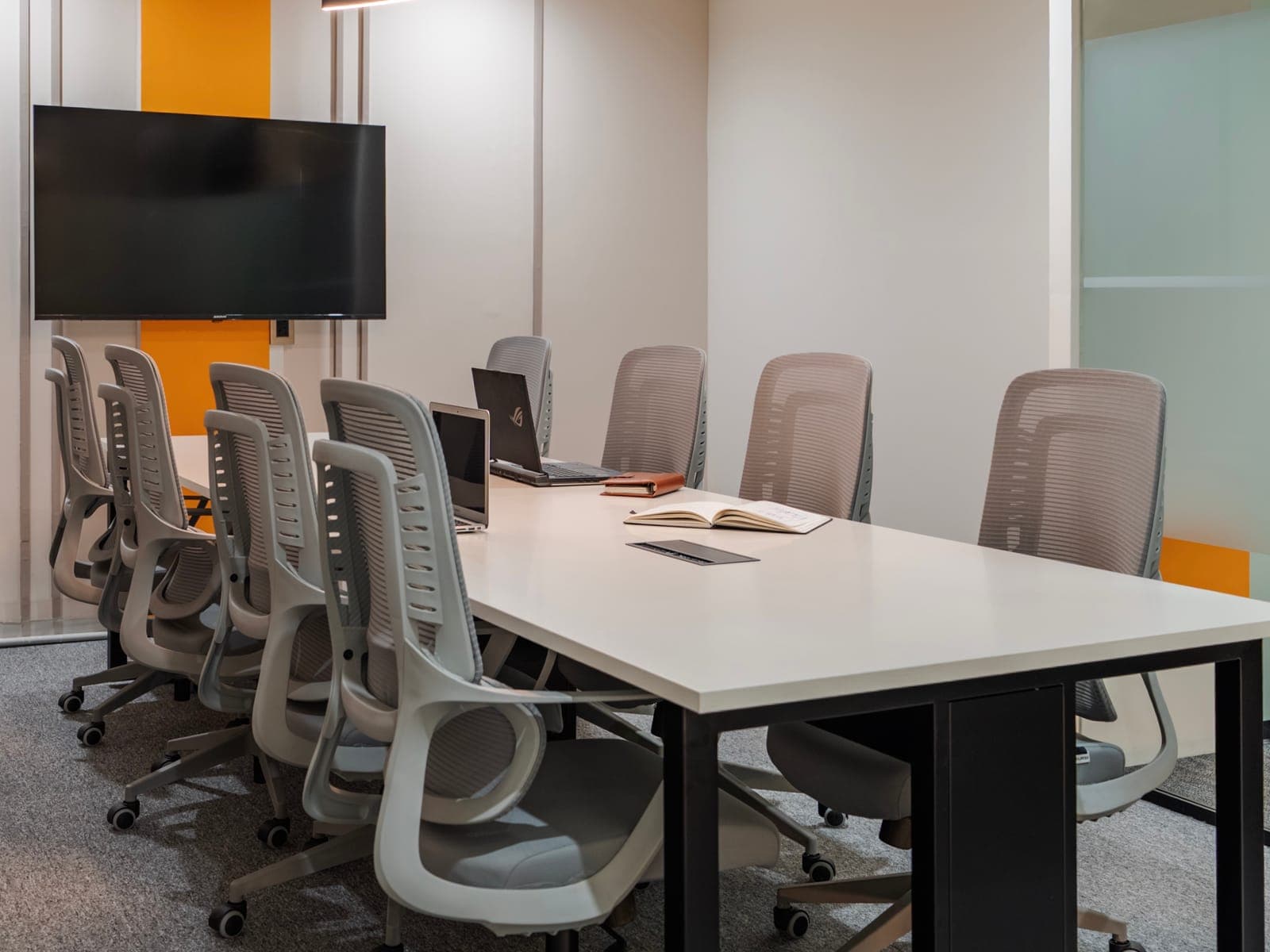 Meeting table with laptops facing the wall-mounted display in the eight-seat meeting room at Fliqzo