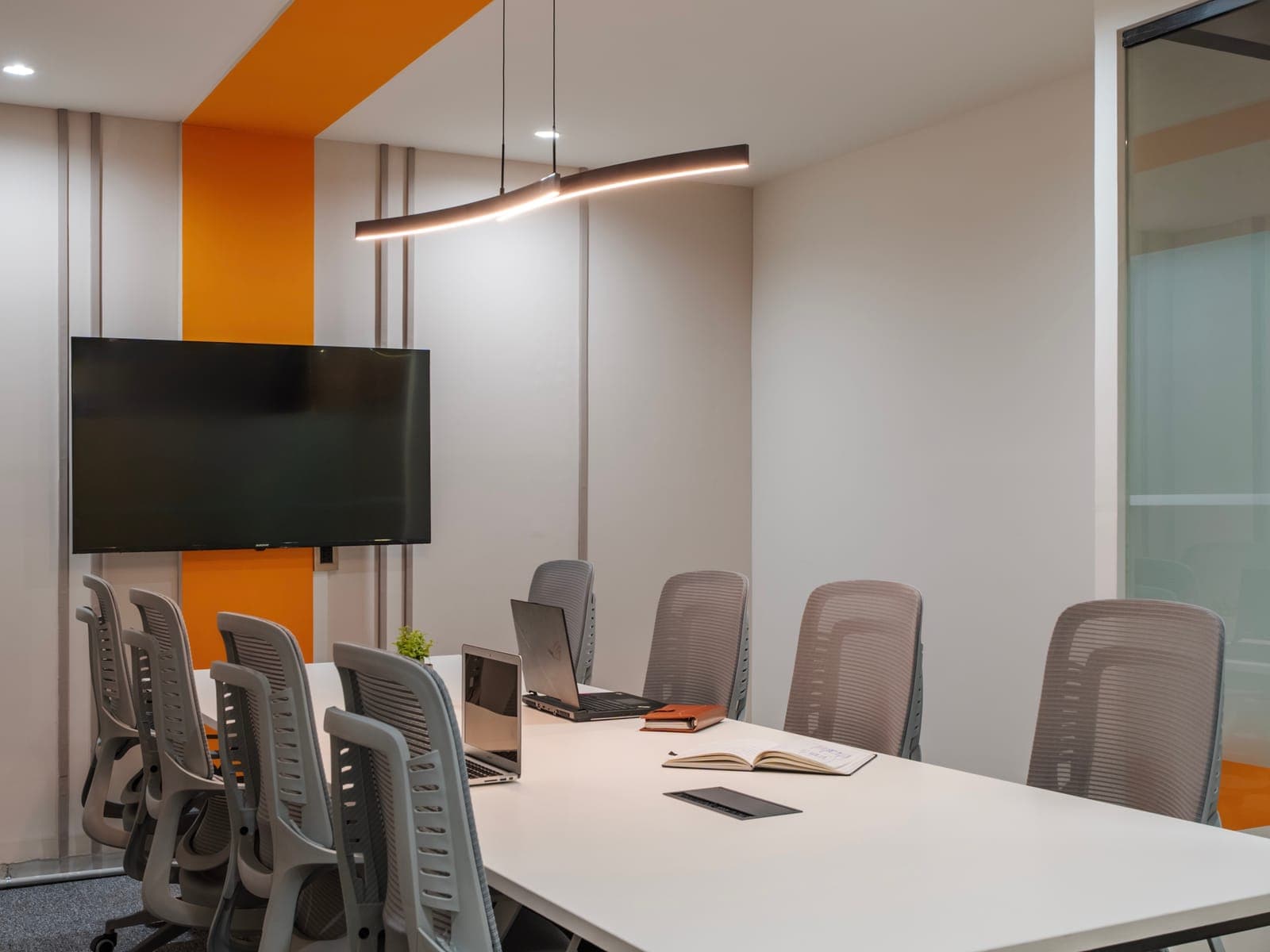 Eight-seat meeting room with wall-mounted display, grey mesh chairs and orange accent ceiling at Fliqzo Coimbatore